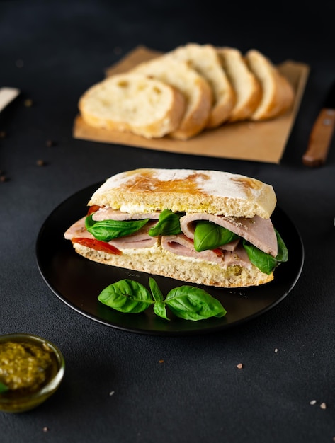 Ciabatta-Sandwich mit Schinken-Pesto-Sauce Tomaten Basilikum auf schwarzem Hintergrund Essen Essen backgroun