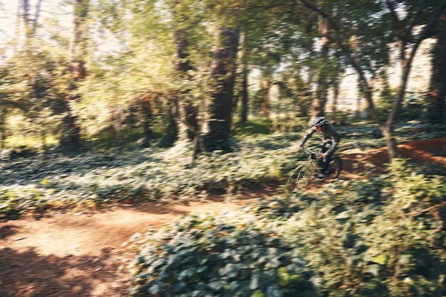 Ciclismo en bicicleta y desenfoque de movimiento con un hombre en el bosque para una aventura de fitness o libertad en la naturaleza Ejercicio en bicicleta y un ciclista masculino al aire libre en el bosque para entrenamiento cardiovascular o de resistencia