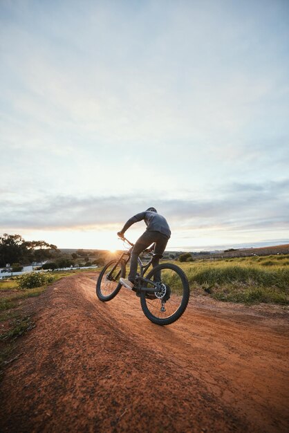 Ciclismo deportivo y hombre en bicicleta en el campo para entrenar y hacer ejercicio en la naturaleza Ciclista de fitness y persona con bicicleta de montaña para la libertad de aventura y andar en camino de tierra al aire libre