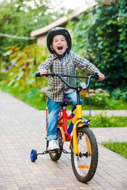 Ciclismo con diversión. Niño alegre manteniendo la boca abierta y expresando positividad mientras monta en bicicleta