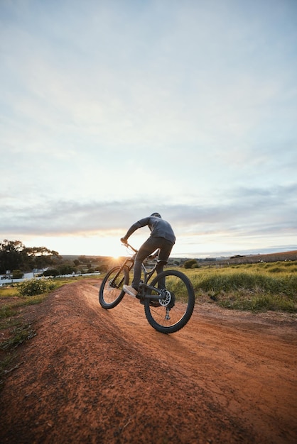 Ciclismo esportivo e homem de bicicleta no campo para treinamento de exercícios e exercícios na natureza Ciclista de fitness e pessoa com mountain bike para liberdade de aventura e passeio na estrada de terra ao ar livre