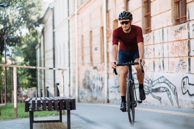 Foto ciclista activo en casco de seguridad y anteojos montando bicicleta negra durante el día soleado al aire libre hombre deportivo que pasa tiempo libre para entrenar en las calles de la ciudad