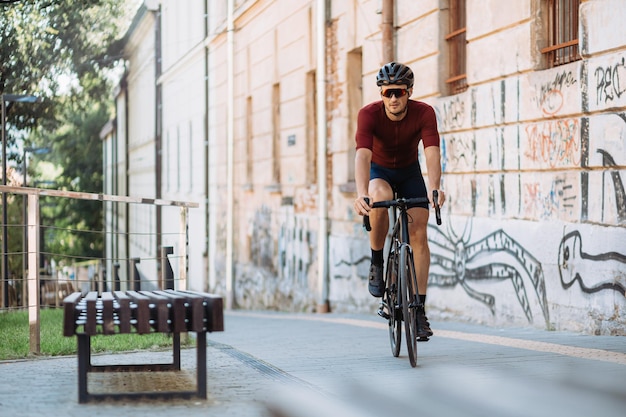 Foto ciclista activo que usa una bicicleta negra para hacer ejercicio al aire libre hombre caucásico en bicicleta cerca de la pared con varios grafitis