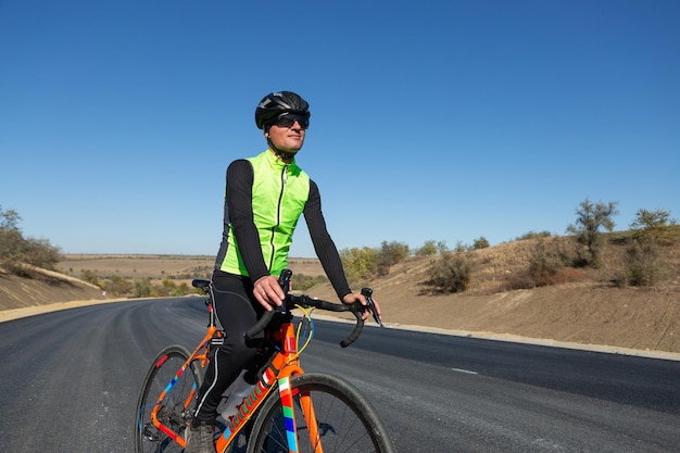 Ciclista andando de bicicleta na estrada contra o céu claro Um homem em uma roupa fica com uma bicicleta em um dia ensolarado de outono