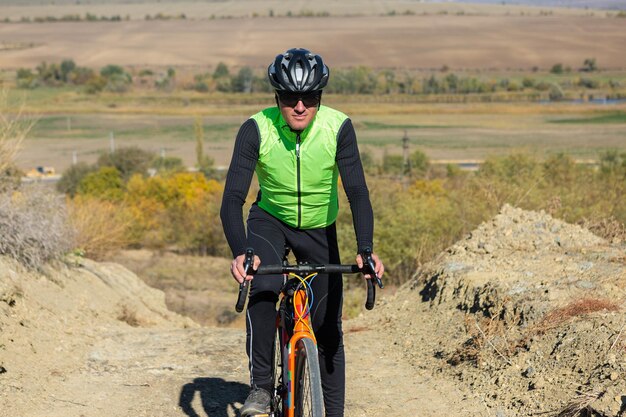 Ciclista andando de bicicleta offroad contra o céu claro Um homem de roupa fica com uma bicicleta em um dia ensolarado de outono