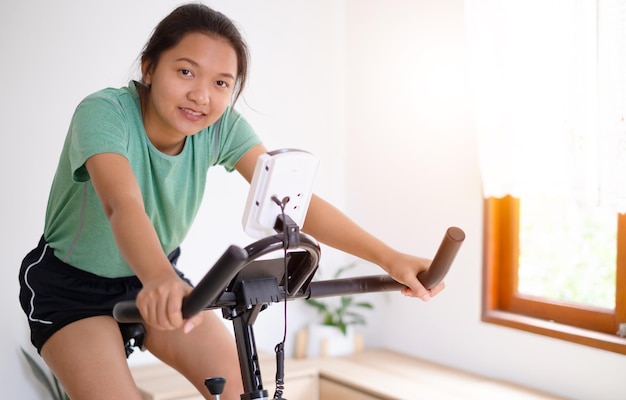 Ciclista asiática Ela está se exercitando na sala de estar em casa