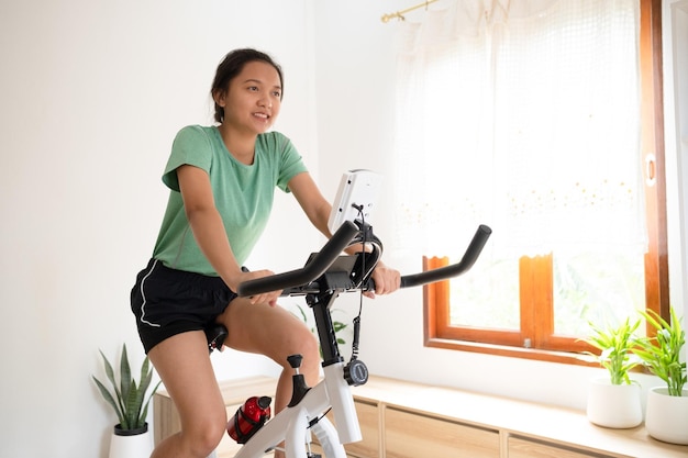 Ciclista asiática Ela está se exercitando na sala de estar em casa