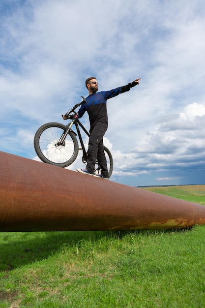 Ciclista barbudo en una bicicleta de montaña en un tubo oxidado hierba verde cielo azul