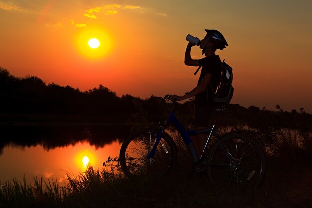 Ciclista en bicicleta agua potable en el fondo del atardecer.