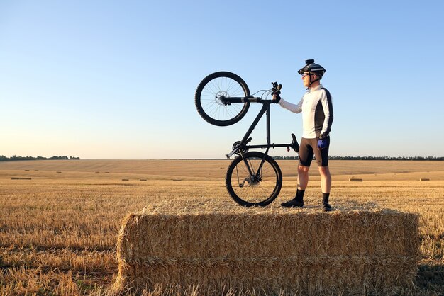 Ciclista con la bicicleta descansando sobre el campo cosechado de paja