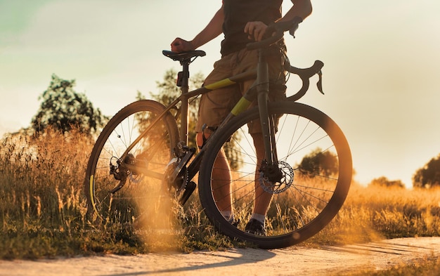 Ciclista con bicicleta en un sendero de tierra al atardecer en el campo hermoso paisaje vespertino con una bicicleta concepto de estilo de vida activo