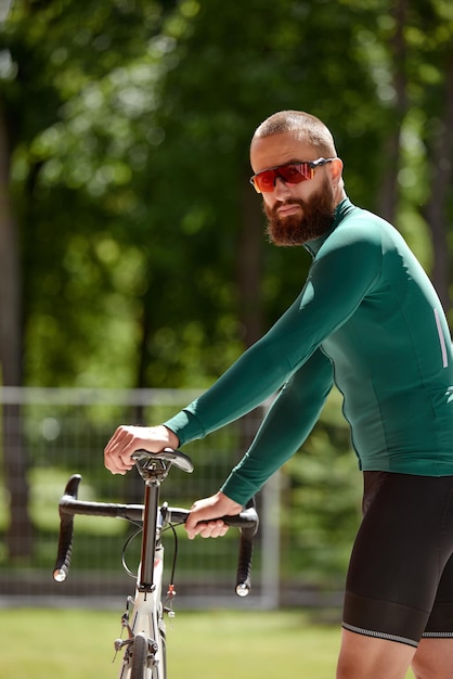 Ciclista caucasiana em roupas esportivas olhando para a câmera enquanto segura uma bicicleta Relaxamento após treinamento ao ar livre