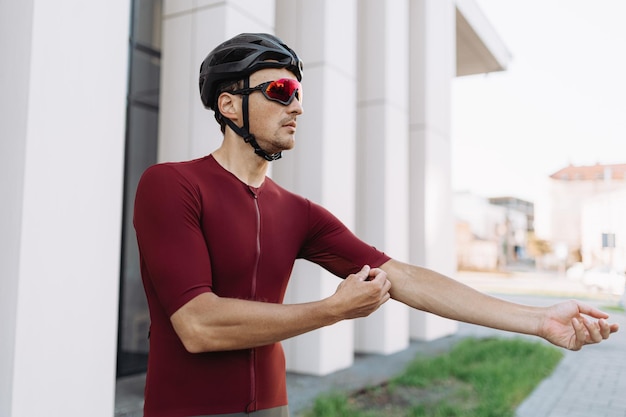 Ciclista caucasiano em capacete e óculos ajustando suas roupas esportivas antes do treino ativo no ar fresco Preparação para treinamento ao ar livre