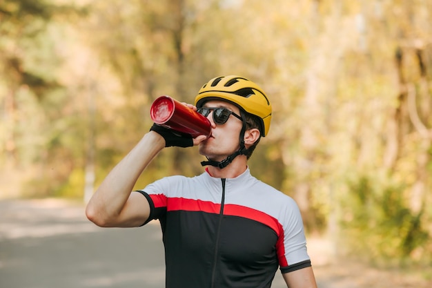 Ciclista com sede bebe água depois de um treino de bicicleta contra o pano de fundo de uma paisagem de outono