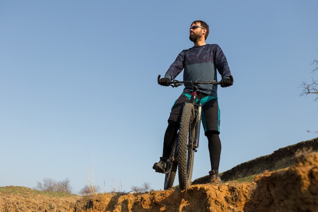 Ciclista de bermuda e malha em uma bicicleta moderna com um garfo de suspensão a ar em um penhasco