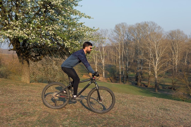 Ciclista de bermuda e malha em uma moderna bicicleta rígida de carbono com um garfo de suspensão a ar em um penhasco contra o fundo de uma floresta verde fresca de primavera