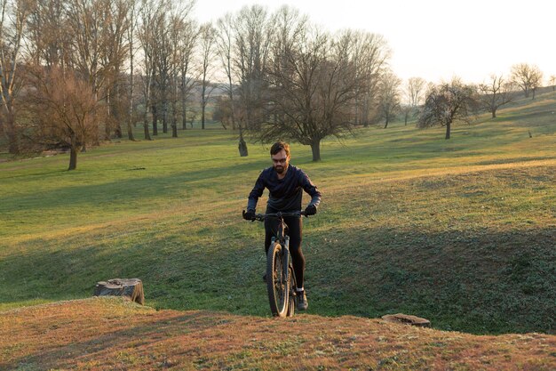 Ciclista de bermuda e malha em uma moderna bicicleta rígida de carbono com um garfo de suspensão a ar em um penhasco contra o fundo de uma floresta verde fresca de primavera