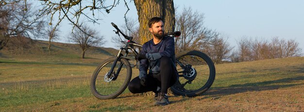 Ciclista de bermuda e malha em uma moderna bicicleta rígida de carbono com um garfo de suspensão a ar em um penhasco contra o fundo de uma floresta verde fresca de primavera