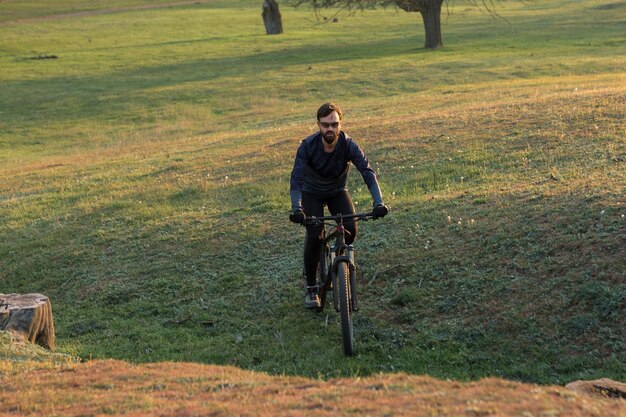 Ciclista de bermuda e malha em uma moderna bicicleta rígida de carbono com um garfo de suspensão a ar em um penhasco contra o fundo de uma floresta verde fresca de primavera