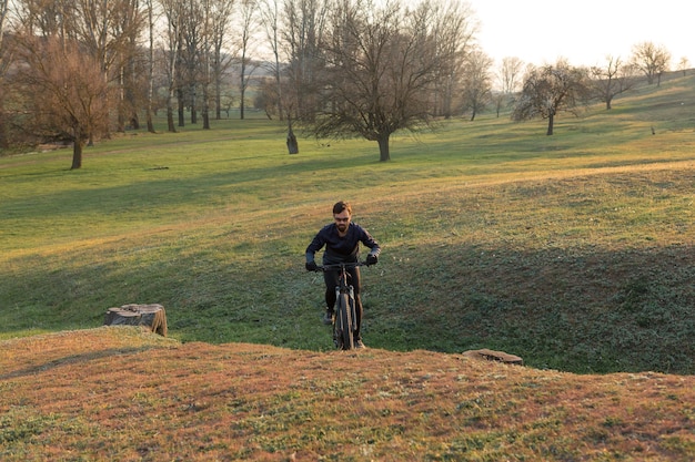 Ciclista de bermuda e malha em uma moderna bicicleta rígida de carbono com um garfo de suspensão a ar em um penhasco contra o fundo de uma floresta verde fresca de primavera