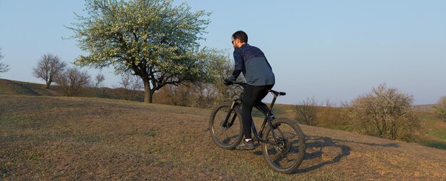 Ciclista de bermuda e malha em uma moderna bicicleta rígida de carbono com um garfo de suspensão a ar em um penhasco contra o fundo de uma floresta verde fresca de primavera