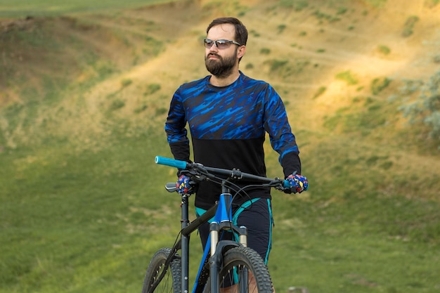 Ciclista de bermuda e malha em uma moderna bicicleta rígida de carbono com um garfo de suspensão a ar em um penhasco contra o fundo de uma floresta verde fresca de primavera