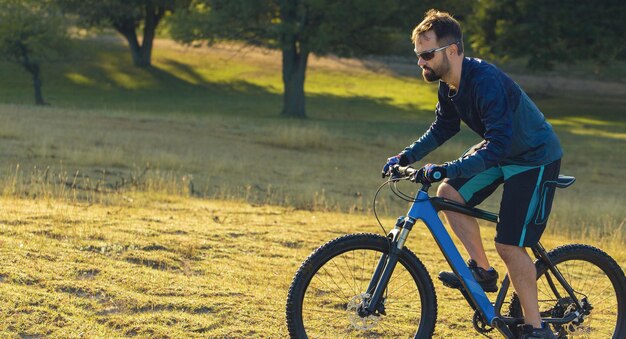 Ciclista de bermuda e malha em uma moderna bicicleta rígida de carbono com um garfo de suspensão a ar em um penhasco contra o fundo de uma floresta verde fresca de primavera