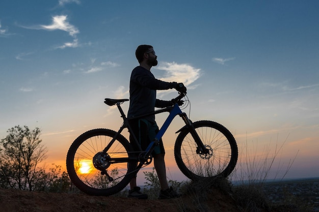 Ciclista de bermuda e malha em uma moderna bicicleta rígida de carbono com um garfo de suspensão a ar em um penhasco contra o fundo de uma floresta verde fresca de primavera