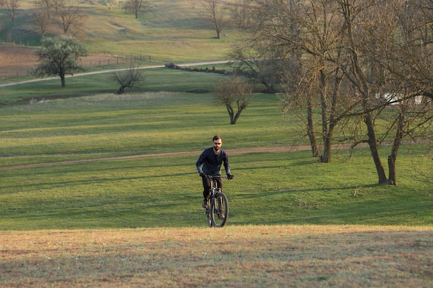 Ciclista de bermuda e malha em uma moderna bicicleta rígida de carbono com um garfo de suspensão a ar em um penhasco contra o fundo de uma floresta verde fresca de primavera