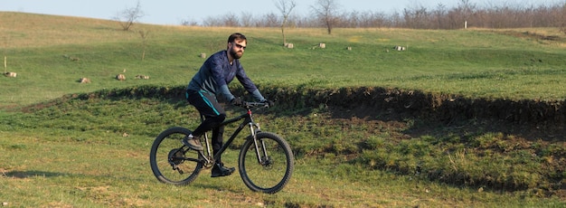 Ciclista de bermuda e malha em uma moderna bicicleta rígida de carbono com um garfo de suspensão a ar em um penhasco contra o fundo de uma floresta verde fresca de primavera