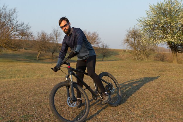 Ciclista de bermuda e malha em uma moderna bicicleta rígida de carbono com um garfo de suspensão a ar em um penhasco contra o fundo de uma floresta verde fresca de primavera