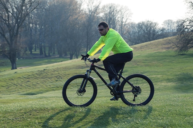 Ciclista de calça e jaqueta verde em uma moderna bicicleta hardtail de carbono com um garfo de suspensão a ar O cara no topo da colina anda de bicicleta