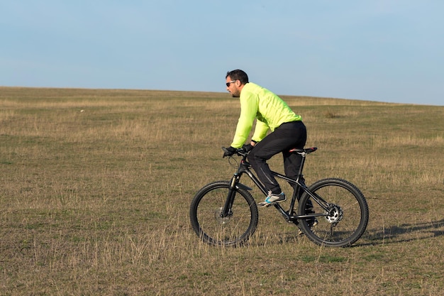 Ciclista de calça e jaqueta verde em uma moderna bicicleta hardtail de carbono com um garfo de suspensão a ar O cara no topo da colina anda de bicicleta