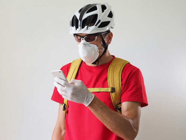 Ciclista de correio no capacete, máscara protetora e luvas médicas, olhando para smartphone