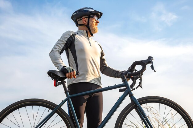 Ciclista de homem barbudo fica com uma bicicleta contra o ciclismo de céu azul e passatempos de saúde