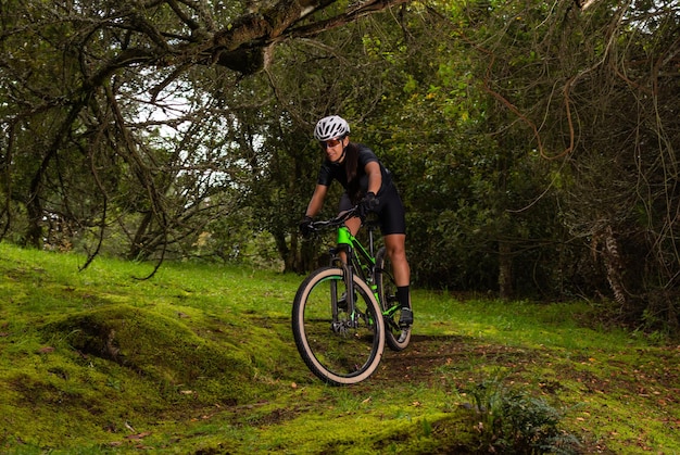 Ciclista de mulher com capacete e óculos em sua bicicleta atravessando uma área arborizada em uma montanha