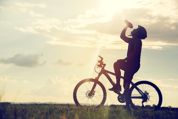 Ciclista descansando y bebiendo agua silueta de ciclismo al atardecer.