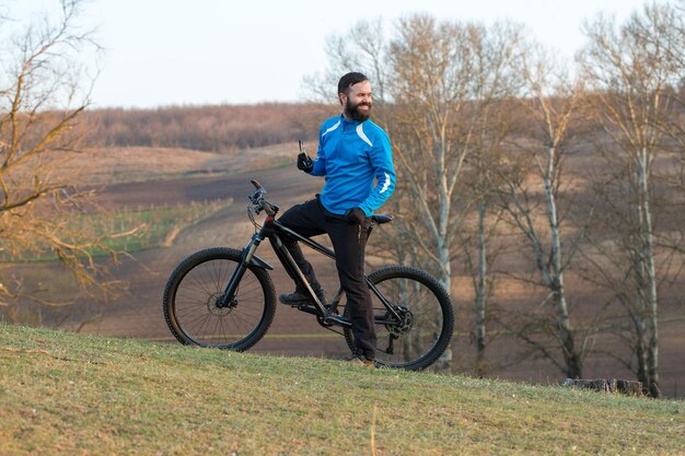 Ciclista em calças e jaqueta de lã em uma moderna bicicleta hardtail de carbono com um garfo de suspensão a ar O cara no topo da colina anda de bicicleta