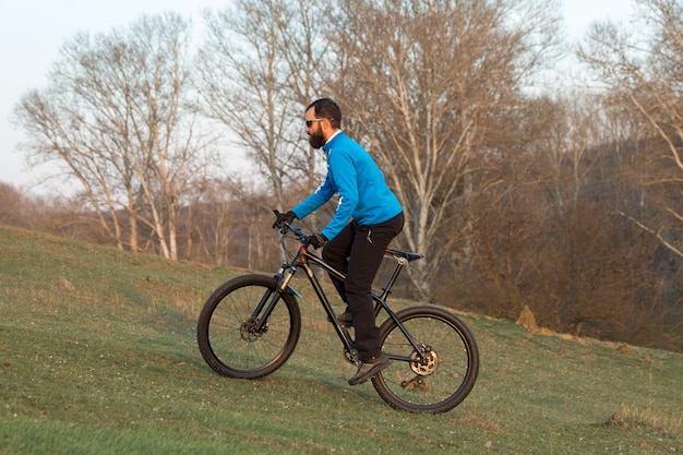 Ciclista em calças e jaqueta de lã em uma moderna bicicleta hardtail de carbono com um garfo de suspensão a ar O cara no topo da colina anda de bicicleta