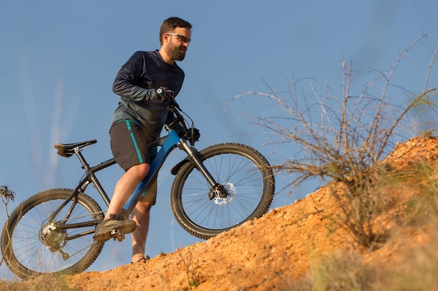 Ciclista em calças e jaqueta de lã em uma moderna bicicleta hardtail de carbono com um garfo de suspensão a ar o cara no topo da colina anda de bicicleta