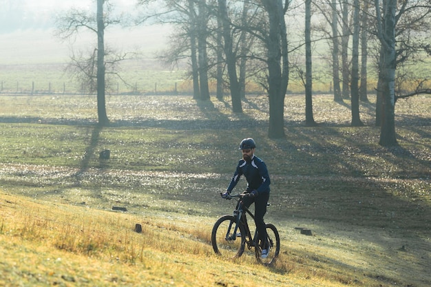 Ciclista em calças e jaqueta de lã em uma moderna bicicleta hardtail de carbono com um garfo de suspensão a ar O cara no topo da colina anda de bicicleta