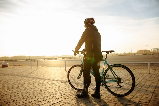 Ciclista em roupas pretas e capacete treina em uma bicicleta