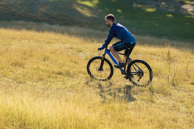 Ciclista em shorts e camisa em uma bicicleta hardtail de carbono moderna com um garfo de suspensão a ar em pé em um penhasco no contexto da floresta verde fresca da primavera