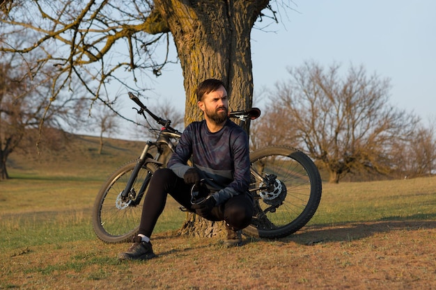 Ciclista em shorts e camisa em uma bicicleta hardtail de carbono moderna com um garfo de suspensão a ar em pé em um penhasco no contexto da floresta verde fresca da primavera