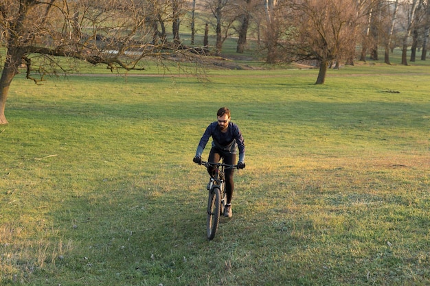 Ciclista em shorts e camisa em uma bicicleta hardtail de carbono moderna com um garfo de suspensão a ar em pé em um penhasco no contexto da floresta verde fresca da primavera