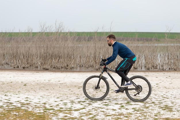 Ciclista em uma bicicleta de montanha em uma praia salgada em um fundo de juncos e um lago