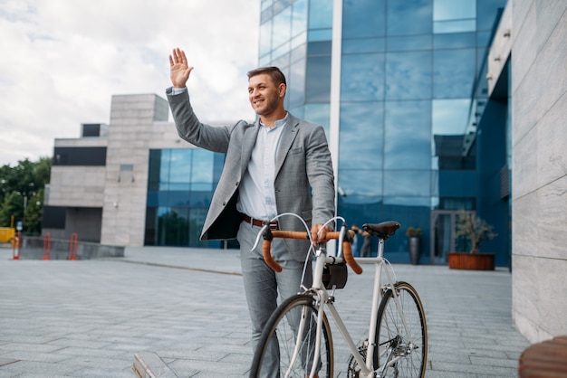 Foto ciclista empresario en traje en el centro de la ciudad, edificio de cristal en el fondo. persona de negocios en transporte ecológico en las calles de la ciudad