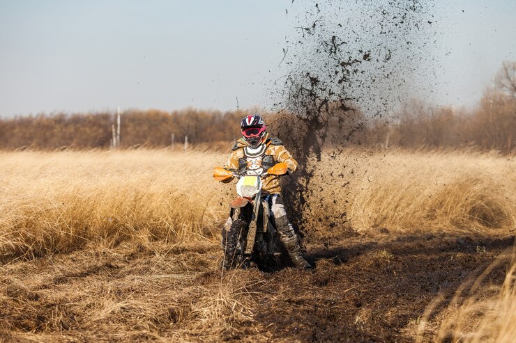Foto ciclista de enduro en un campo con pasto seco en otoño. la motocicleta patina y hace muchas salpicaduras de barro.