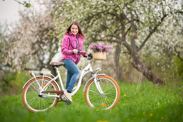 Ciclista femenina con bicicleta blanca vintage en jardín de primavera