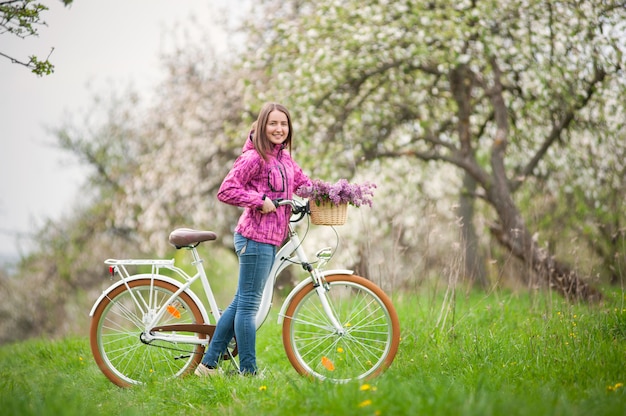 Ciclista femenina con bicicleta blanca vintage en jardín de primavera